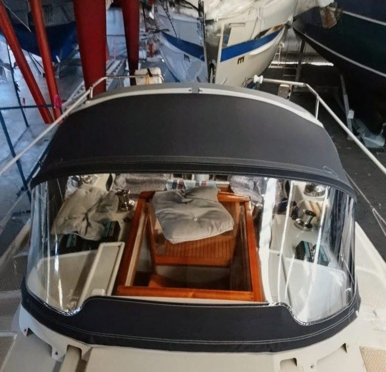 Maßgeschneiderte Sprayhood und Kuchenbude Eine passgenaue, dunkelgraue Sprayhood mit geräumiger Kuchenbude auf einem Segelboot, maßgefertigt vom Segelmacher für optimalen Wetterschut